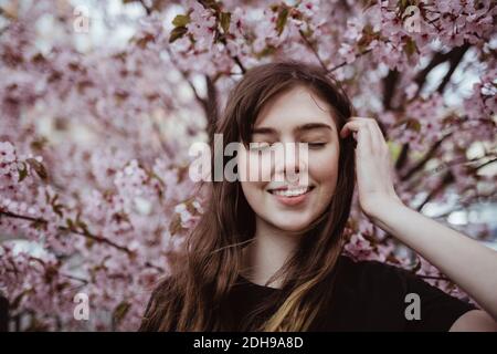 Smiling woman with eyes closed standing against tree Stock Photo