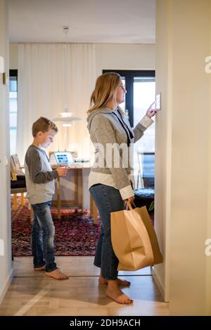 Mother with shopping bag using digital tablet on wall while son standing at home Stock Photo