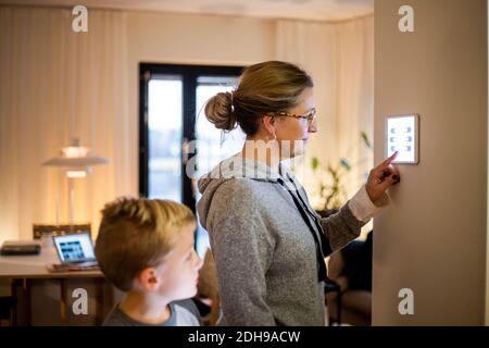 Son looking at mother using digital tablet mounted on wall at smart home Stock Photo