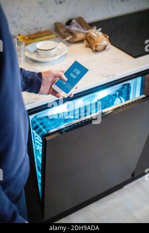 Cropped image of man using mobile app while standing by dishwasher at smart home Stock Photo