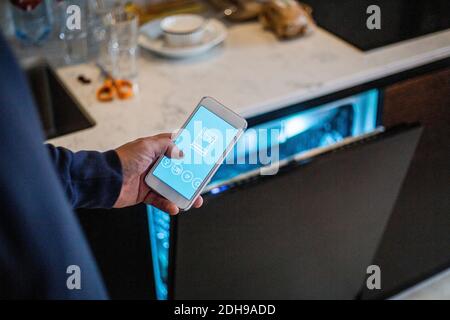Cropped image of man using mobile app against dishwasher at smart home Stock Photo