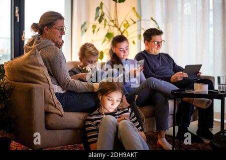 Parents sitting with children while using wireless technologies in living room at modern home Stock Photo