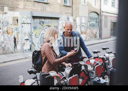 Couple using mobile phones at bicycle sharing system Stock Photo