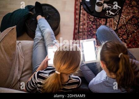High angle view of sisters using wireless technologies while sitting on sofa at home Stock Photo