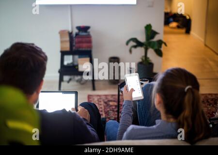 Father and daughter using wireless technologies while relaxing on sofa at smart home Stock Photo