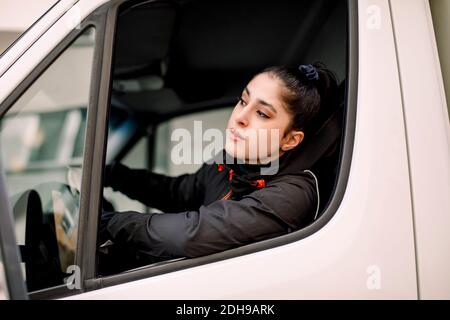 Young delivery woman looking through window while driving truck Stock Photo