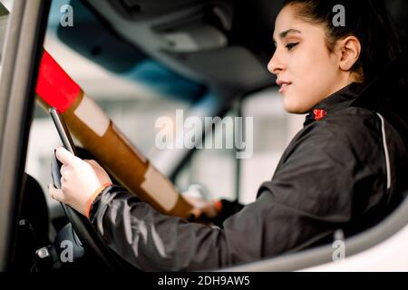 Young delivery woman using smart phone while driving truck Stock Photo