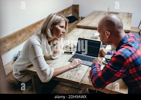 Multi-ethnic couple discussing while using laptop at table in coffee shop Stock Photo