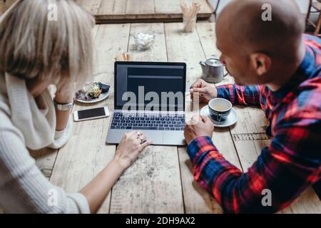 Multi-ethnic couple using laptop at table in coffee shop Stock Photo