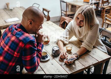 Multi-ethnic couple using mobile phone at table in coffee shop Stock Photo