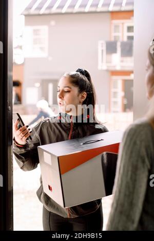 Delivery young woman using mobile phone while delivering package to customer Stock Photo