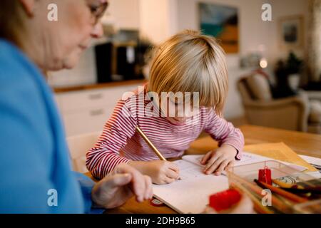 Boy doing homework by grandmother at table Stock Photo