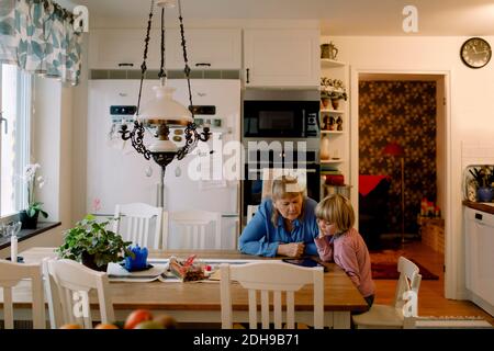 Grandmother and grandson using digital tablet while sitting at dining table Stock Photo