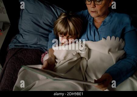 High angle view of grandmother reading story book for grandson on bed at home Stock Photo