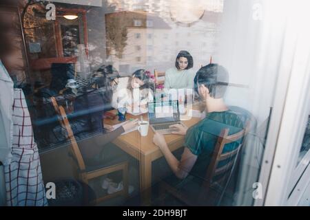 Young friends studying together in dorm room seen through glass window Stock Photo