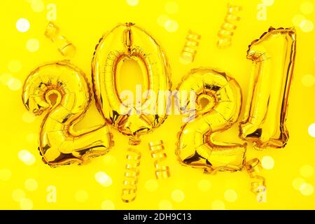 Happy New 2021 Year. Holiday gold metallic balloon numbers 2021 and falling serpentine on yellow background. Gold foil balloons numeral 2021 Stock Photo