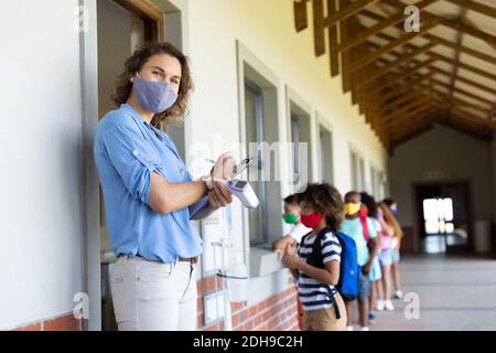 Portrait of female teacher wearing face mask with clipboard and temperature gun Stock Photo