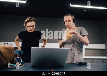 Young androgynous colleagues looking at laptop while standing in office Stock Photo