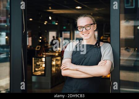 Portrait of smiling andorgynous owner standing with arms crossed at cafe doorway Stock Photo