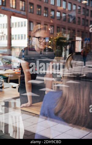 Smiling young transgender barista talking with female customer seen through cafe window Stock Photo