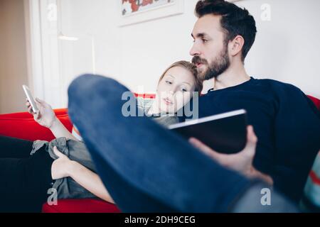 Couple using technologies while sitting on sofa in living room at home Stock Photo