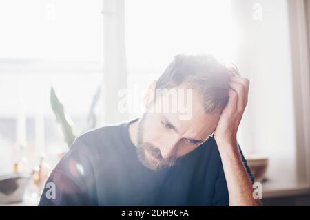 Worried man sitting with head in hands against window at home Stock Photo
