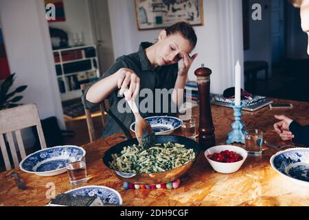 Woman holding wooden spoon in pasta on dining table at home Stock Photo