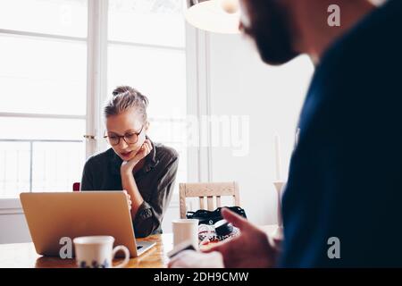 Midsection of man by woman using laptop against window at home Stock Photo