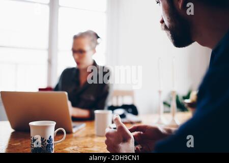 Cropped image of man looking at woman using laptop against window Stock Photo