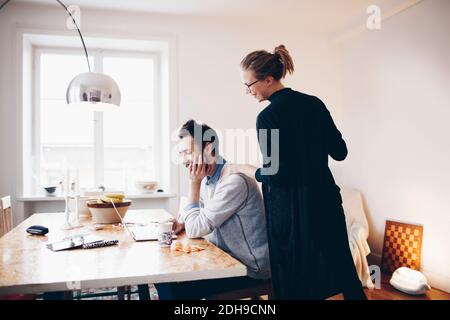 Happy couple looking at laptop on dining table in room Stock Photo
