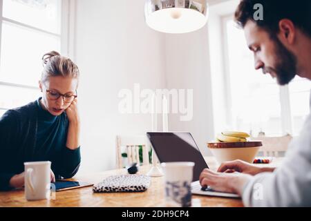 Couple using technologies at dining table while working from home Stock Photo