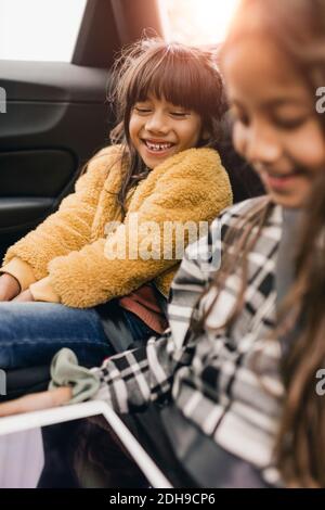 Smiling sisters using digital tablet while traveling in electric car Stock Photo