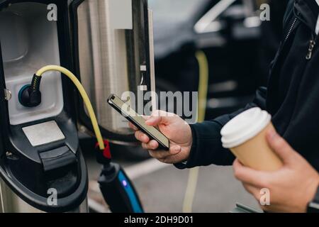 Midsection of man using smart phone at electric car charging station Stock Photo
