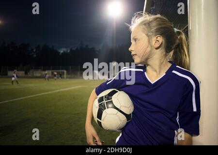 Girl holding soccer ball standing by goal post on field Stock Photo