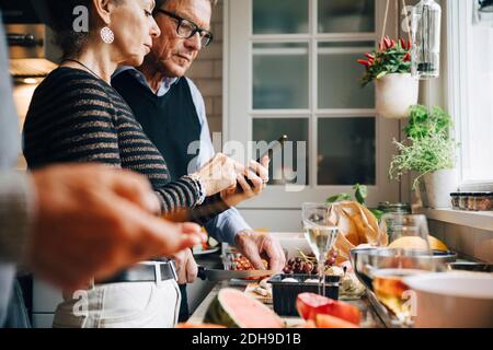Senior woman showing smart phone to man while preparing dinner in kitchen Stock Photo