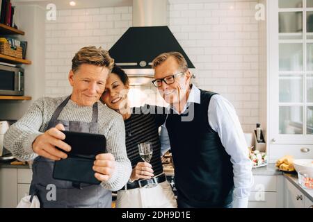 Smiling man taking selfie with friends standing in kitchen at home Stock Photo