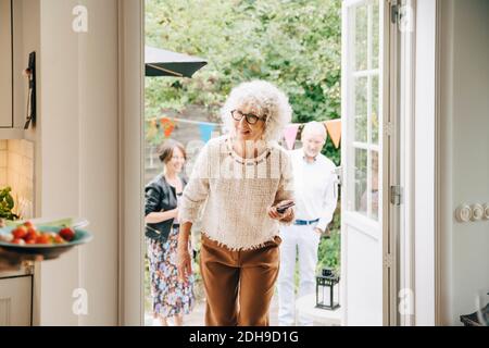 Smiling woman with curly white hair walking through doorway against friends Stock Photo