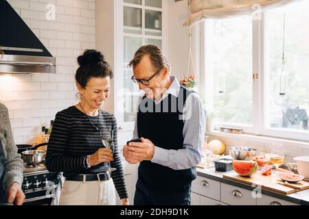 Smiling man and woman sharing smart phone while standing in kitchen Stock Photo