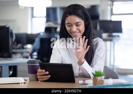 Businesswoman wearing headset waving while having a video chat on digital tablet Stock Photo