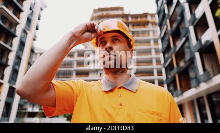 Construction worker putting on his safety gear helmet at job site. Safety first, profession concept. Builder puts on hard hat un Stock Photo