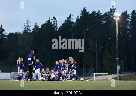 Coach standing with girls soccer team on field against trees Stock Photo