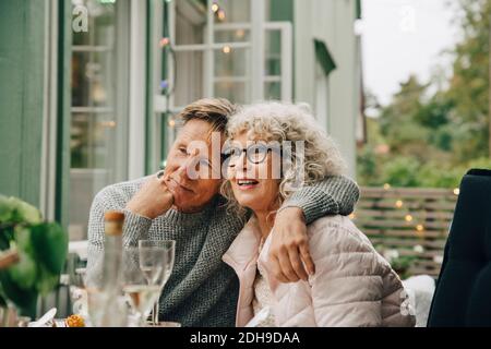 Thoughtful senior man sitting with arm around woman at dining table during garden party Stock Photo