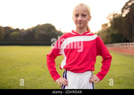 Portrait of confident girl standing with hands on hip at soccer field Stock Photo