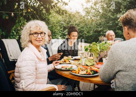 Portrait of smiling senior woman sitting with friends at dining table during dinner party Stock Photo