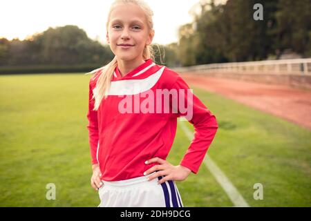 Portrait of confident girl standing with hands on hip at soccer field Stock Photo