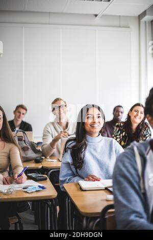 Multi-ethnic smiling male and female students sitting at desk in classroom Stock Photo