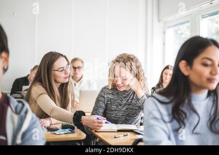 Female students discussing over book at desk in classroom Stock Photo