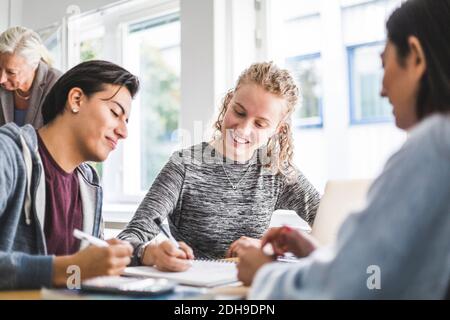 Smiling young woman discussing with male friend over book in classroom Stock Photo