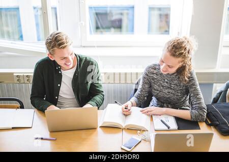 Smiling male and female students studying at desk in classroom Stock Photo