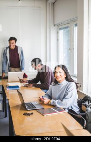 Smiling young woman looking away while sitting at desk in classroom Stock Photo